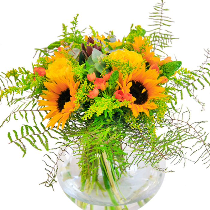 A dazzling harvest-inspired floral arrangement, this sunflower and rose bouquet captures the radiant energy of South Norwood in bloom. Front and center, brilliant sunflowers-petals fanning out in a halo of gold-are juxtaposed with sumptuous yellow garden roses, their tightly layered blossoms opening with a sense of gentle anticipation. Highlights of deep green foliage and airy sprays of golden rod fill out the bouquet, creating movement that recalls the lively pathways of South Norwood Lakes on a breezy afternoon. Here and there, glossy red Hypericum berries nestle among the leaves, sparking visual interest and invoking the cheerful ambiance of the local farmers' market. Wispy ferns tumble over the rim of a perfectly clear, globe-like glass vase, where a tangle of fresh stems is beautifully displayed beneath the shimmering surface of clean water. Peeking from between lush greens, muted blue eucalyptus leaves lend a whisper of woodland calm to the mix. The arrangement as a whole radiates optimism and generosity, with a scent that hints of fresh earth and sun-warmed fields. Whether gracing a dining table for a joyful reunion or brightening a sunlit window along Portland Road, this bouquet-available for prompt delivery throughout South Norwood-brings the spirit of natural beauty and heartfelt celebration into any home.
